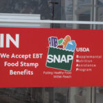 A red sign in store door with SNAP logo and "We accept EBT Food Stamp Benefits"