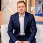 Spencer Pratt sits on a studio couch leaning forward.