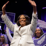 D.C. Democrat mayoral primary winner Janeese Lewis George in white pant suit waves both hands to supporters.