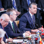Secretary of War Pete Hegseth speaks while at a table alongside fellow NATO defense ministers.