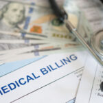 A fanned-out batch of $100 bills on top of a bill reading "Medical Billing" next to a stethoscope.