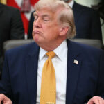 A frowning President Trump sits at his Oval Office desk.