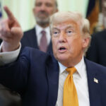President Trump points with his left hand while sitting in the Oval Office.