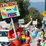 A male teacher carries a sign reading "Teaching With Pride" during a Pride Parade.