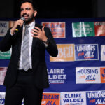 Zohran Mamdani on a stage in front of a slew of political posters.