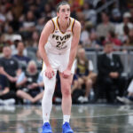 Caitlin Clark rests her hands on her thighs in the middle of a basketball court.