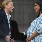 A very pregnant Usha Vance in a white and blue dress speaks to someone at a World Cup match.