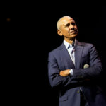 Barack Obama, with his arms folded, against a black background.