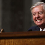 A smiling Lindsey Graham sits in a Senate hearing.