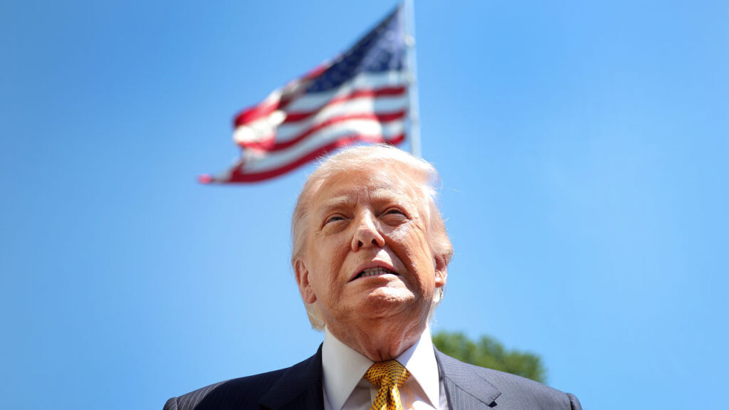 Low angle close-up of President Trump, with an American flag waiving above his head.