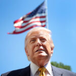 Low angle close-up of President Trump, with an American flag waiving above his head.