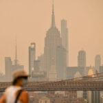 A person wearing a facemark walks near the Brooklyn Bridge as wildfire smoke from Canada causes hazy conditions on July 16, 2026 in New York. Out-of-control wildfires were raging Thursday in the Canadian province of Ontario, prompting evacuations and sending dangerous smoke billowing into the United States where millions of people were exposed to the unhealthy air.