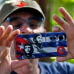 A member of the Nuestra America Convoy takes a photo with his mobile phone, whose case features images of slain Argentine-born Cuban revolutionary Ernesto "Che" Guevara and late Cuban leader Fidel Castro over a Cuban flag, during an event at the Cuban Institute of Friendship with the Peoples (ICAP) in Havana on March 21, 2026. (Photo by Ernesto Mastrascusa / POOL / AFP via Getty Images)