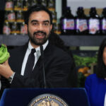 New York City Mayor Zohran Mamdani holds up bananas as he speaks at a food distribution center on July 27, 2026 in the Brooklyn borough of New York City. Mamdani announced that the five upcoming city-owned grocery stores will offer a 30 percent discount on produce, meat, bread, and milk when they begin to open next year. The discount on essential items will potentially save shoppers an estimated $90 a month, or roughly $1,000 a year, as prices for food and other items continue to rise throughout the country. The mayor has pledged one community grocery store for each borough. (Photo by Spencer Platt/Getty Images)