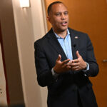 Hakeem Jeffries in suit speaks to a woman in front of a NABJ conference welcome sign in a hallway.