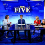 Four of the hosts of "The Five," joined by a laughing JD Vance, sit around a circular news desk on the set of The Five, with blue backgrounds and the show’s logo—highlighting America 250—displayed behind them.