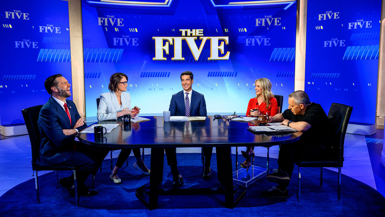 Four of the hosts of "The Five," joined by a laughing JD Vance, sit around a circular news desk on the set of The Five, with blue backgrounds and the show’s logo—highlighting America 250—displayed behind them.