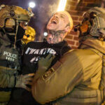 Federal agents with Homeland Security Investigations (HSI) detain a protestor wearing an "Antifa" shirt.