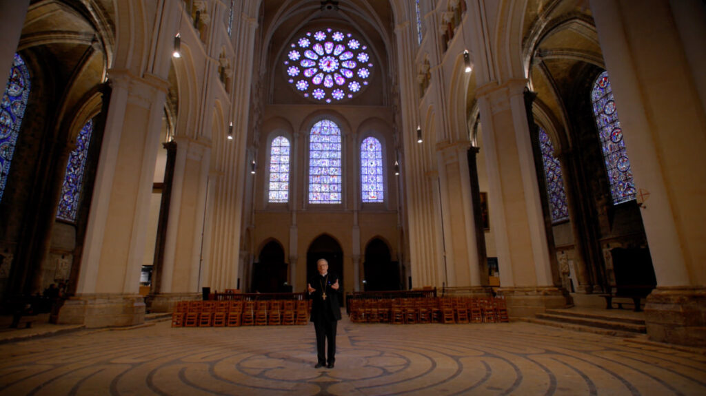 Bishop Barron’s First Theatrical Film Isn’t Nostalgia. It’s a Challenge. 4 A person stands in the center of a grand cathedral with tall columns, stained glass windows, and intricate circular designs on the floor.