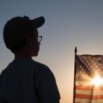 Silhouette of a boy with a setting sun shining through an American flag.