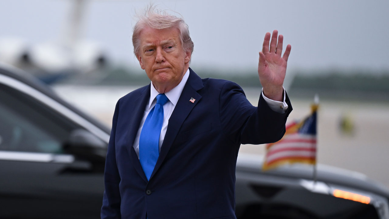 President Donald Trump waves to reporters at an airport.