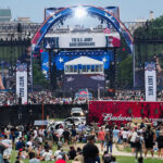 Crowd gathered for Freedom 250 event, with red, white and blue stage in the background.