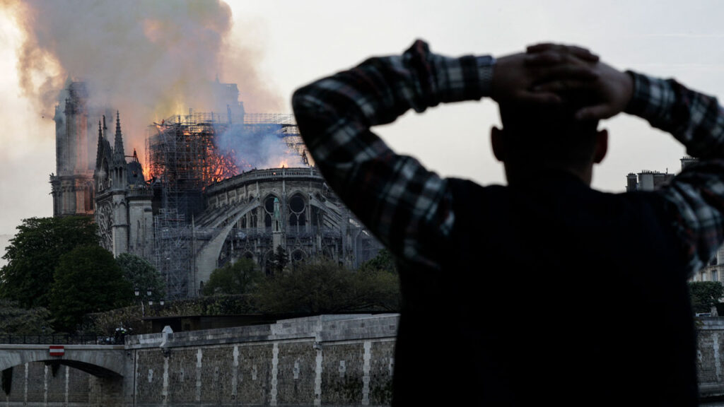 Bishop Barron’s First Theatrical Film Isn’t Nostalgia. It’s a Challenge. 1 A person stands on the riverbank with hands on their head, watching smoke and flames rise from the burning Notre-Dame Cathedral in Paris.