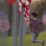 A boy runs among U.S. flags in a field