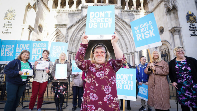 Girl standing with a sign saying, "Don't Screen Us Out."