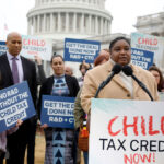 A woman speaks with a "CHILD TAX CREDIT NOW!" sign in front of her and the U.S. Capitol in the background.