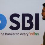 A man walks past an SBI logo and slogan, The banker to every Indian, displayed on a white wall.