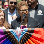 Los Angeles Mayor Karen Bass stands at a podium draped with pride colors.