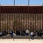 Migrants sit by the iron fence waiting to be processed by the U.S. Border Patrol near the Jacumba Hot Springs after crossing the border.