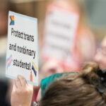 A person holds a sign reading, "Protect trans and nonbinary students!"