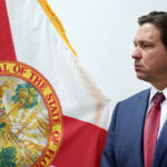 Governor Ron DeSantis standing in front of Florida flag.