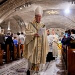 A Catholic bishop and altar server process at the end of Mass in a crowded church