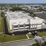 Aerial view of a large, modern data center building with the Cologix logo, surrounded by parking lots, roads, trees, and nearby industrial and residential areas.