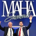 Two men in suits stand side by side, smiling and waving, in front of a blue backdrop with large white text that says “MAHA Summit.”.