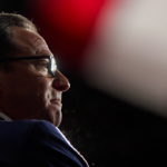 Gov. Shapiro shown in profile against a dark background with bright red and white blurred lights, evoking an educational atmosphere reminiscent of a lecturer or scholar deep in thought.