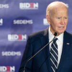 Former President Joe Biden stands at a microphone, with a banner featuring his name and that of "SCDEMS."