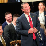 U.S. Rep. Ronny Jackson (R-TX) March 20, 2026 stands laughing amid a group of seated individuals.