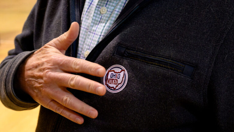 A man places his hand by the "Ohio Voted" sticker on his suit jacket.