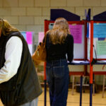 Three people stand at separate voting booths in a room, filling out ballots.
