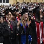 Graduates in robes clapping, cheering, and smiling