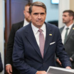 Acting Attorney General Todd Blanche looks right at the camera as he arrives for a hearing with files in his hand.