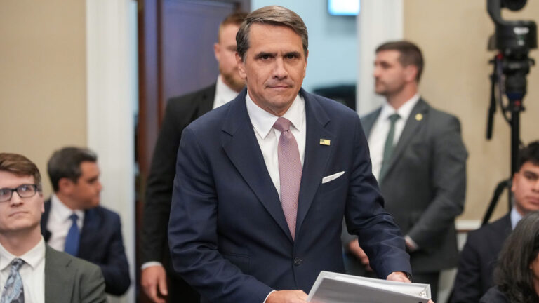 Acting Attorney General Todd Blanche looks right at the camera as he arrives for a hearing with files in his hand.