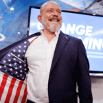 Steve Hilton stands on stage at his election night event smiling.
