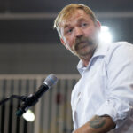 Democrat Graham Platner looks off to the side as he speaks at a podium.