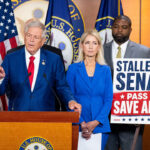 Rep. Ralph Norman of South Carolina Stands at the center of a podium, while other members and a sign urging passage of the SAVE America Act are beside him.