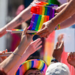Someone leans over to hand a crowd of people rainbow pride flags during a parade.